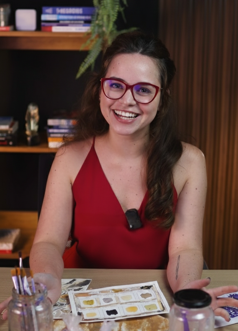 Artista sorrindo em seu ateliê com aquarelas e pincéis sobre a mesa